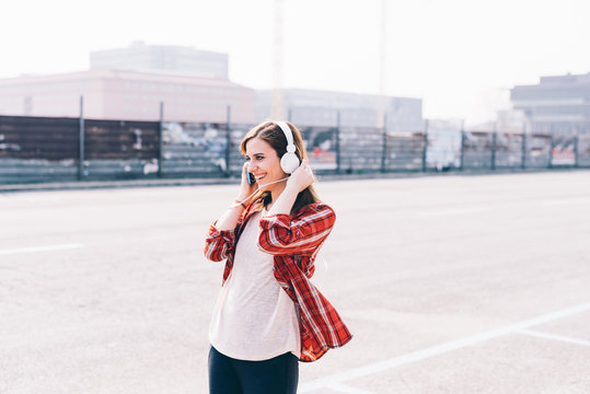 Young woman outdoor in the city listening music with headphones and smartphone hand hold - music, relaxing, technology concept