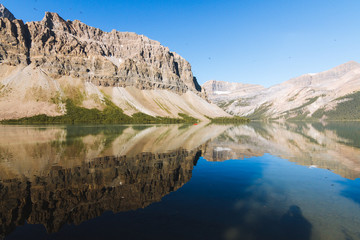 People on canoe on Bow Lake with reflection on water in Rocky Mountains, Alberta during sunrise on sunny day