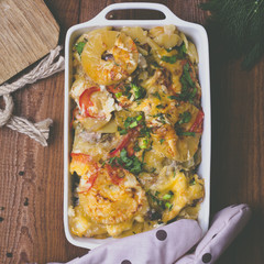 Potato gratin with cream, cheese, tomatoes, meat, pineapple, parsley in the baking dish. Flat lay. Tonned image.