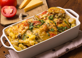 Potato gratin with cream, cheese, tomatoes, meat, pineapple, parsley in the baking dish. 