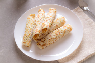 Homemade crepes with cream soft cheese on white plate, cup of coffee. Sunny morning. Delicious breakfast.