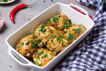 Chicken thighs gratin with sour cream and cheese, parsley, garlic, chilli pepper in the white baking dish.