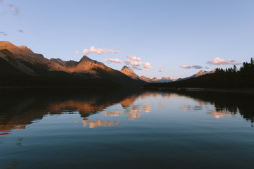 Reflections on Maligne lake in Rocky Mountains during colorful sunset with clouds