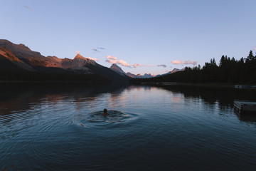 Man swimming in Maligne lake in Rocky Mountains during colorful sunset with clouds - 187620017