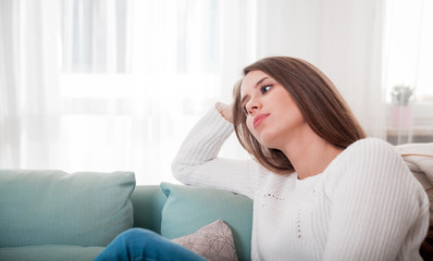 Naklejka premium Sad woman sitting on sofa at home deep in thoughts, thinking concept