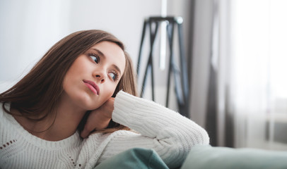 Sad woman sitting on sofa at home deep in thoughts, thinking concept