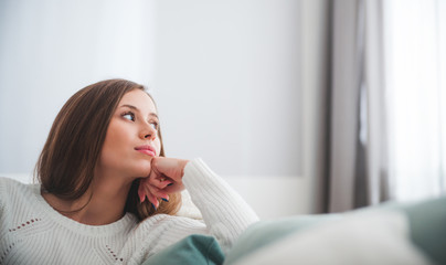 Sad woman sitting on sofa at home deep in thoughts, thinking concept