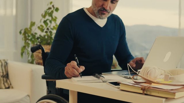 Mature man in wheelchair working in home office.