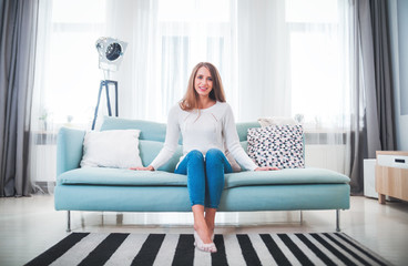 Pretty woman at home sitting on sofa in modern interior