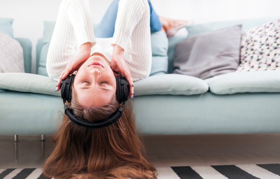 Woman with headphones on sofa at home listening music