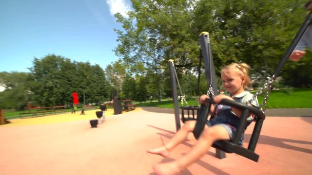 Mother rides her little daughter on swing at playground 4K