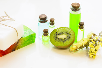 Fruit aromatherapy concept with essential oil in bottles, soap, kiwi and flower, white background, close up