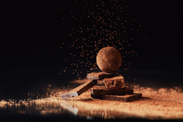close up view of truffle on chocolate bars with cocoa powder on black - obrazy, fototapety, plakaty