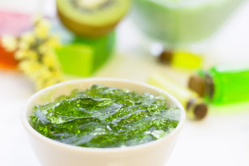 Natural green cosmetics concept. A container of jelly cream soap, kiwi and bottles of essential oil, white background, top view