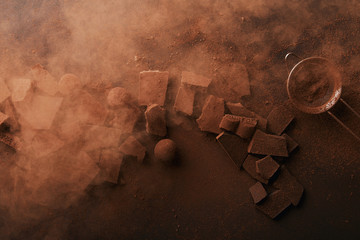 top view of arrangement of various types of chocolate, truffles and sieve with cocoa powder