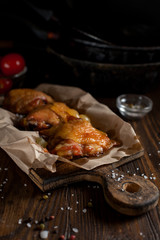 baked juicy chicken with a crispy crust, in spices, on a black plate, on baking paper, large sea salt on a dark wooden background