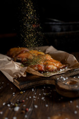 baked juicy chicken with a crispy crust, in spices, on a black plate, on baking paper, large sea salt on a dark wooden background