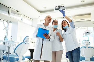 Group of dentists examining x-ray image of patients teeth. Standing in new bright dentist office.