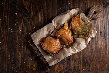 baked juicy chicken with a crispy crust, in spices, on a black plate, on baking paper, large sea salt on a dark wooden background