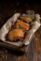 baked juicy chicken with a crispy crust, in spices, on a black plate, on baking paper, large sea salt on a dark wooden background