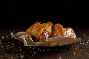 baked juicy chicken with a crispy crust, in spices, on a black plate, on baking paper, large sea salt on a dark wooden background