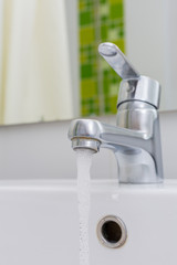 Modern chrome tap faucet with running water.