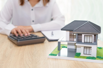 Woman calculating about installment price with estate loan agreement document and home model