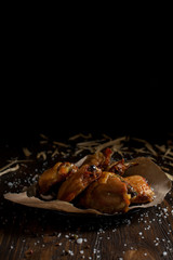 baked juicy chicken with a crispy crust, in spices, on a black plate, on baking paper, large sea salt and large wood chips on a dark wooden background