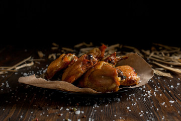 baked juicy chicken with a crispy crust, in spices, on a black plate, on baking paper, large sea salt and large wood chips on a dark wooden background