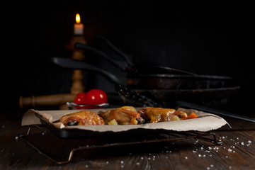 baked juicy chicken with a crispy crust, in spices, on a black plate, on baking paper, large sea salt on a dark wooden background