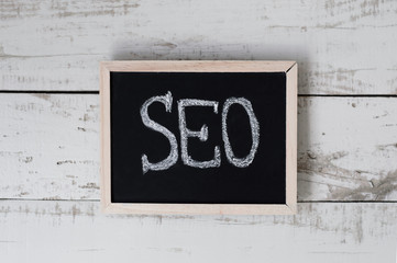 Small blackboard with handwritten text "SEO" on gray wooden background, top view. Search engine optimization concept. Digital marketing
