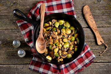 Fried Brussels sprouts with mushrooms and nuts on a cast-iron frying pan on a wooden background.