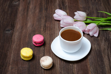 Fototapeta na wymiar Cup of coffee, macarons and pink tulips on wooden background. Top view