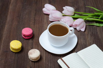 Fototapeta na wymiar Cup of tea, macarons, pink tulips and notebook on wooden background.