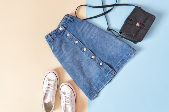 Fashionable concept. Female urban style. Denim skirt, handbag and white sneakers on a blue background, beige