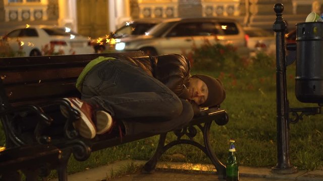 Drunk Man sleeping on the Bench in the City Near the Rubbish Bin.