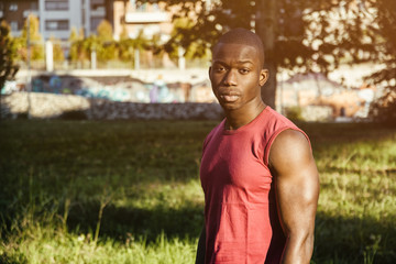 Fototapeta premium Portrait of a sexy young black man in urban park, wearing red sleeveless shirt