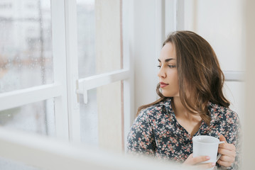 Beautiful woman looking through window on rainy day.