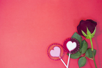 The concept of St.Valentine's Day red background with a beautiful red rose and lolipop candies, top view, copy space
