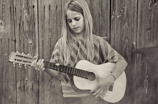 young girl playing guitar by old rustic wooden barn with fog in sepia tones
