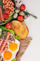 English breakfast tomatoes, sausages, beans, mushrooms, eggs,toast and herbs top view. On a white wooden background.