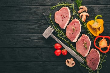 Beef steak with fresh vegetables and rosemary and spices on a black wooden background. Top view. Free space for text.