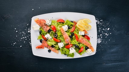 Salmon salad, feta cheese, salad leaves and fresh vegetables on the plate. On a wooden background. Top view. Free space for text.