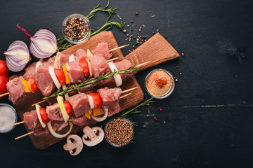 Raw kebab from meat on a wooden background with vegetables. Top view. Free space for text.