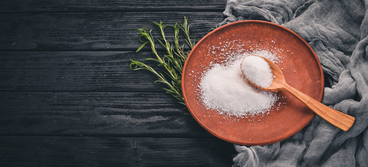 Salt in a wooden spoon on a plate. On a wooden background. Top view. Free space for text.
