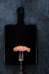 Slices Steak Ribeye on meat fork on a black cutting board