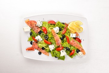 Salmon salad, feta cheese, salad leaves and fresh vegetables on the plate. On a wooden background. Top view. Free space for text.