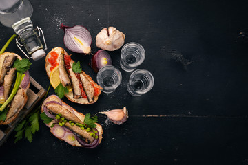 Vodka and a set of sandwiches with sprats, and caviar, onion and parsley, on a wooden background....