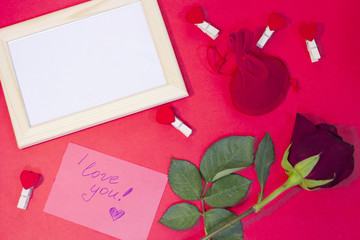 The concept of St.Valentine's Day with a beautiful red rose, a love note and wooden photo frame, red background, top view