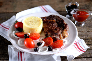Beef steak with mashed potatoes and salad of cherry tomatoes, dried olives and white onions.